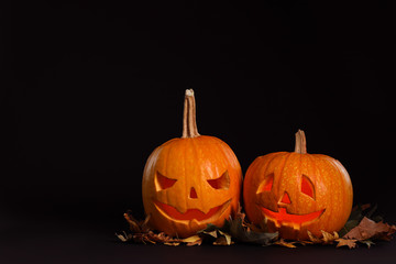 Pumpkin heads with autumn leaves on black background, space for text. Jack lantern - traditional Halloween decor