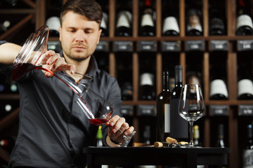 Sommelier pouring wine into glass from mixing bowl. Male waiter