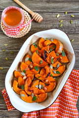 Pumpkin slices baked in the oven with honey, nuts, cinnamon, seeds, mint. Pieces of pumpkin lying on the baking paper in a bowl. Healthy food, dessert for gourmets. Traditional autumn snack in Hungary
