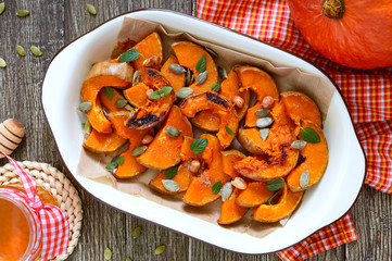 Pumpkin slices baked in the oven with honey, nuts, cinnamon, seeds, mint. Pieces of pumpkin lying on the baking paper in a bowl. Healthy food, dessert for gourmets. Traditional autumn snack in Hungary