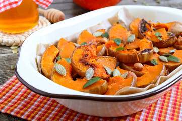 Pumpkin slices baked in the oven with honey, nuts, cinnamon, seeds, mint. Pieces of pumpkin lying on the baking paper in a bowl. Healthy food, dessert for gourmets. Traditional autumn snack in Hungary
