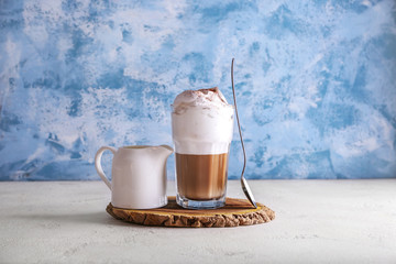 Glass of tasty frappe coffee and jug of milk on table