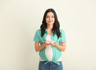 Beautiful young pregnant woman with baby booties on light background