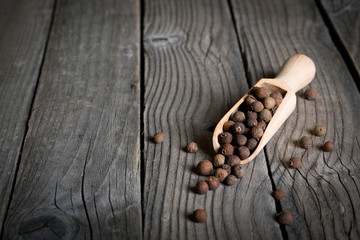 Pepper peas in a wooden spoon on a wooden background. Spices are scattered on the table
