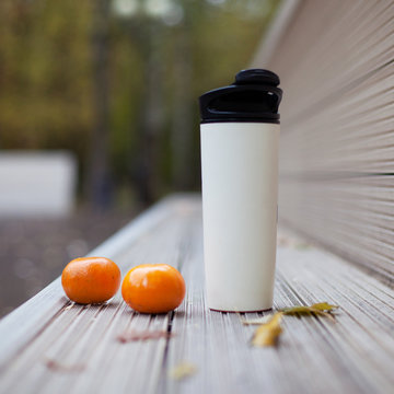 Plastic thermo Cup with hot drink and tangerines on a bench in the autumn Park