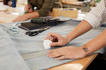 Close-up of tailor holding chalk and drawing pattern with ruler on fabric for future dress at the...