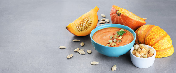 Pumpkin cream soup with croutons and seeds over gray texture.