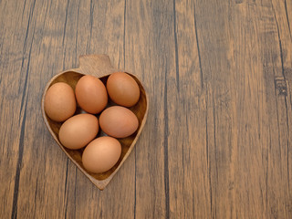 Eggs in the wooden bowl heart shape on the wooden table. top view.
