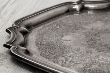 Antique tarnished silver tray with engraved pattern on a grey wood background