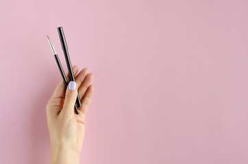 Hand with makeup brush and pencil composition on pink background.