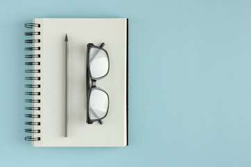 Note pad with eyeglasses and pencil composition on blue background.