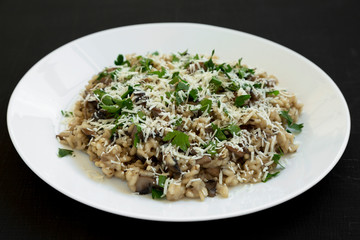 Homemade mushroom risotto on a white plate on a black surface, side view.