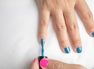 Close-up of female hands painting blue nail varnish, self made manicure at home.