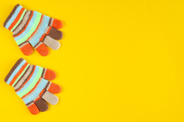 Striped kids winted gloves composition on yellow background.