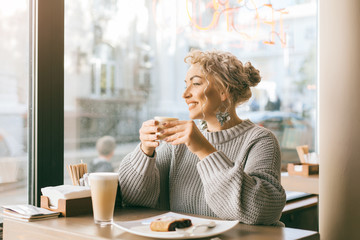 Woman drinking coffe by the window in city street cafe