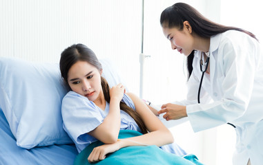 Fototapeta premium Asian young female doctor with syringe to the arm of Asian young female patient on Bed for better healing In the room hospital background.