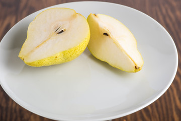 half and a quarter of a yellow pear on a white plate