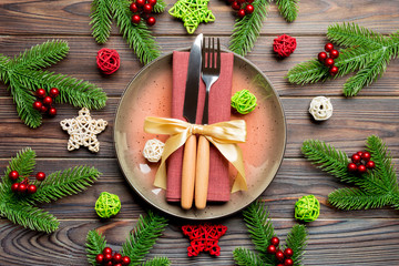 Holiday composition of plate and flatware decorated with Santa hat on wooden background. Top view of Christmas decorations. Festive time concept