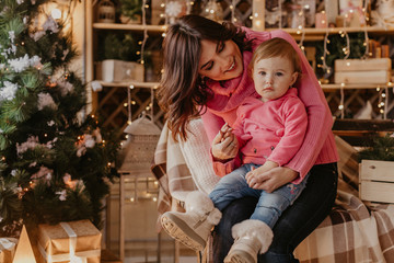 Smiling mother playing with lovely baby near Christmas tree - Image