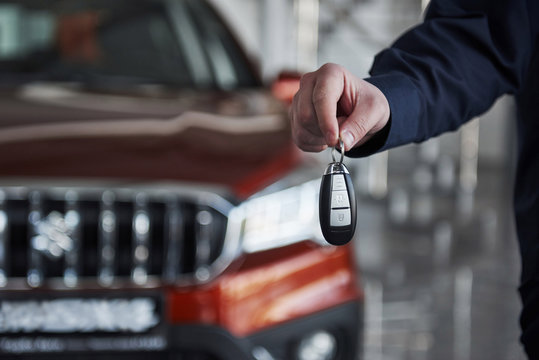 Close up view of man's hand holds keys from brand new red car that stands at background