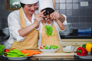 Asian woman young mother with son boy cooking salad mom sliced vegetables food son tasting salad dressing vegetable carrots and tomatoes bell peppers happy family cook food enjoyment lifestyle kitchen