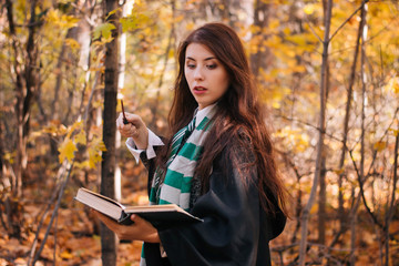 Schoolgirl of magic with a magic wand and a thick book in her hands in the autumn forest. The young...