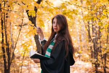 Schoolgirl of magic with a magic wand and a thick book in her hands in the autumn forest. The young...