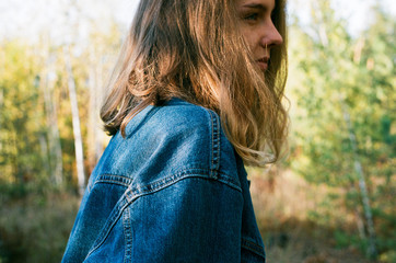 The blonde in a denim vest against the background of the autumn forest