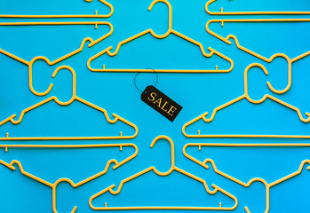 Many empty yellow hangers racks with tag on bright blue color table background, retail male female clothes fashion store shopping sale season wardrobe promotion cheap offer concept, top above view