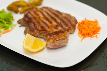 Juicy and delicious grilled meat steak with lemon, carrots, lettuce and potatoes.