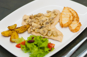 Stewed mushrooms with fish fillet, salad, fried potatoes and croutons, close-up. Tasty traditional italian food