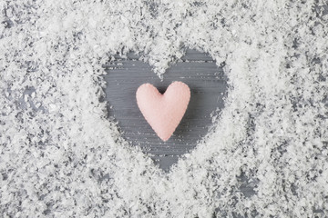 Pink heart between decorative snow on wooden desk