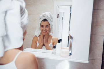 Satisfied with results. In the bathroom. Woman in white towel in head have care of herself