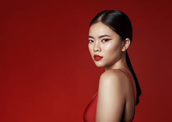 Beauty asian girl with creative make-up. Red eyeliner and red lips. A woman is standing on a red background.