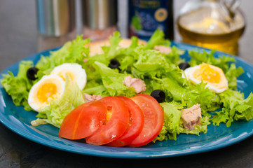Salad with tuna, eggs, tomato, olives, spices and croutons, sauce or oil on blue plate