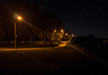 Night park with luminous lanterns. Contrasting yellow light.