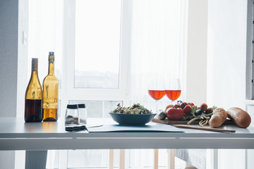 Near the window. Photo of vegetables, salad and two glasses with red wine at the table