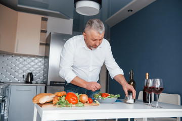 Picking some salt. Man in white shirt preparing food on the kitchen using vegetables