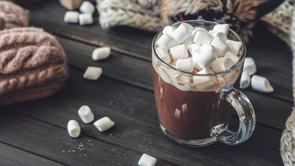 Hot cocoa with marshmallows in a glass cup surrounded by Christmas gifts and winter clothes, Christmas atmosphere and coziness