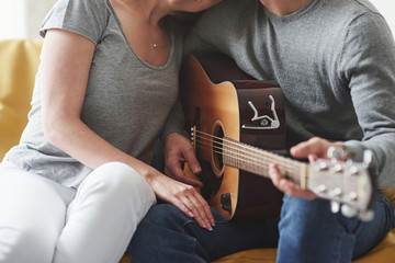 Casual clothes. Playing on acoustic guitar for the girlfriend in the living room of new house