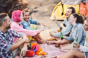 Happy friends having fun camping outdoor - Young people drinking beers and playing guitar in campsite next the beach - Youth culture and travel vacation concept