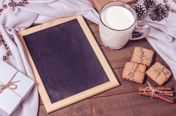 A cup of milk, cinnamon sticks, homemade biscuits and a slate in Christmas decor.