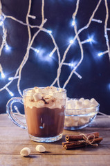 Hot chocolate, cinnamon sticks and marshmallow on the background of burning garlands, Christmas decorations, close up