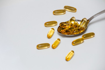a metal spoon filled with omega 3 fish oil capsules, omega 3 fish oil capsules are scattered around...