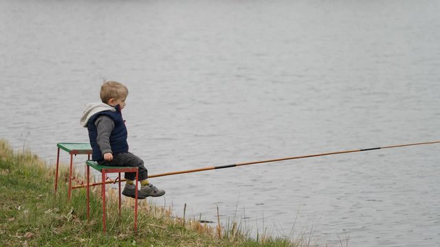 Little child fishing alone on lake shore