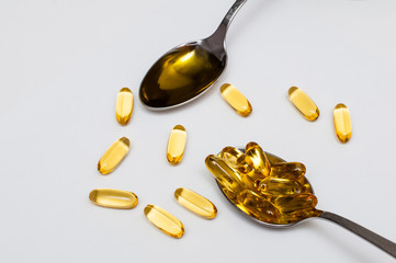 confrontation of omega 3 fish oil in capsules against omega 3 fish oil in liquid form, metal spoons...