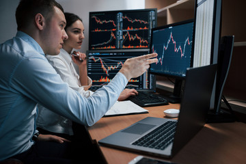 Man talks and shows on the numbers on monitor with hand. Team of stockbrokers are having a...