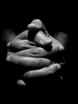 Black an white close up of a mans clasped hands in low key lighting