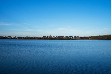 A lake with blue water and sky. Beautiful houses and cottages on the horizon.
