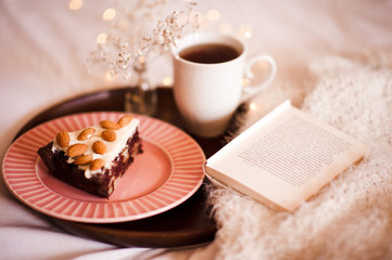 Choolate pie with almond nuts, open book, cup of coffee on wooden tray in bed closeup. Good morning.